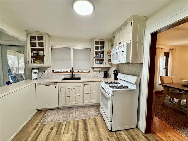 kitchen with white appliances, light countertops, backsplash, light wood finished floors, and a sink