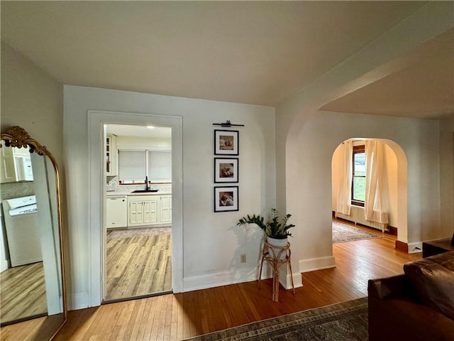 hallway featuring radiator, arched walkways, light wood-style flooring, and a sink