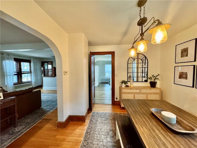 hallway with radiator, wood finished floors, baseboards, and arched walkways