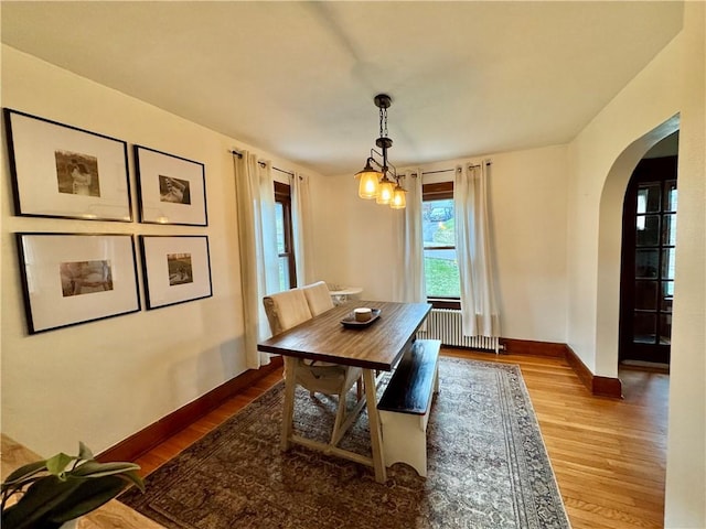 dining area with radiator heating unit, wood finished floors, baseboards, and arched walkways
