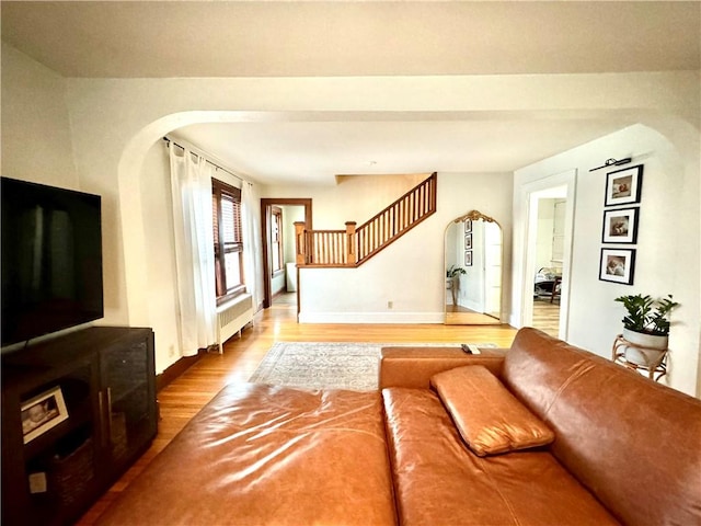 living room featuring baseboards, stairway, wood finished floors, and radiator heating unit