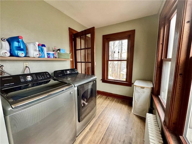clothes washing area featuring washing machine and clothes dryer, baseboards, radiator, light wood-type flooring, and laundry area