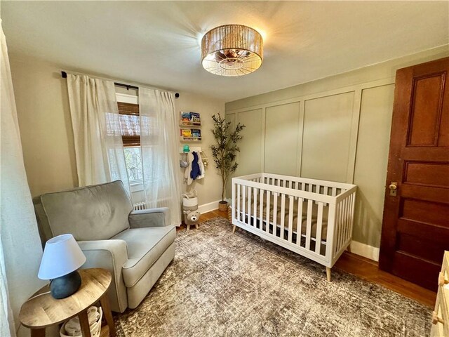 bedroom with baseboards, a nursery area, and wood finished floors