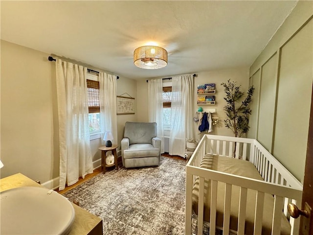 bedroom featuring baseboards, a crib, wood finished floors, and radiator heating unit