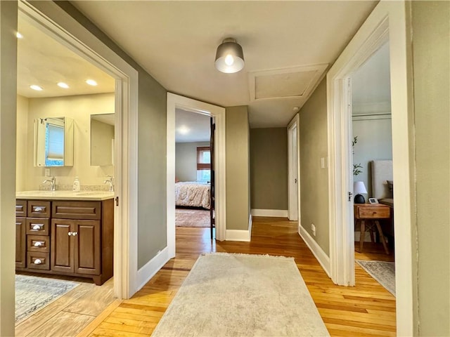 hall featuring attic access, a sink, baseboards, and light wood-style floors