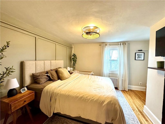 bedroom featuring light wood-type flooring, baseboards, and radiator