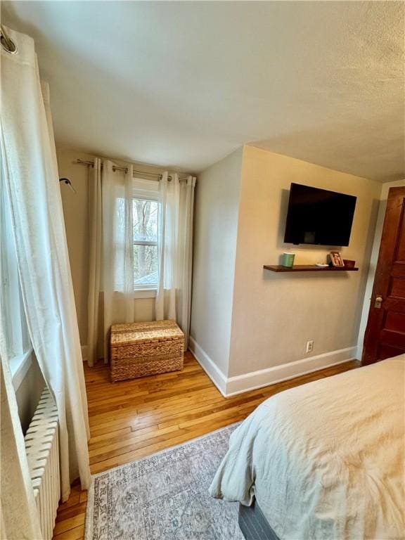 bedroom with light wood-type flooring, radiator heating unit, and baseboards