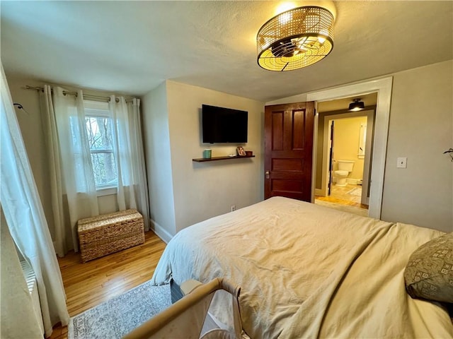 bedroom with wood finished floors, connected bathroom, and baseboards