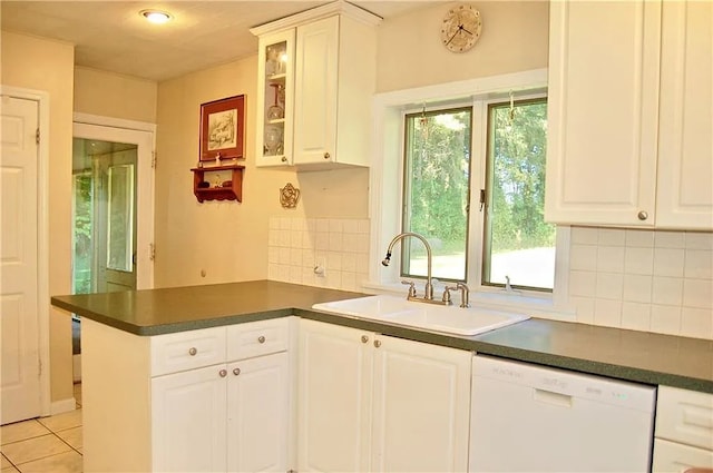 kitchen with white dishwasher, dark countertops, a sink, a peninsula, and decorative backsplash