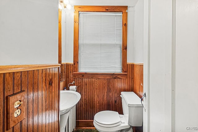 half bathroom featuring wainscoting, toilet, wooden walls, and a sink