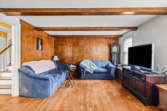 living area featuring stairway, beamed ceiling, wood walls, and light wood-style flooring