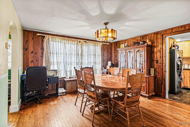 dining space with arched walkways, an inviting chandelier, wood walls, and hardwood / wood-style floors
