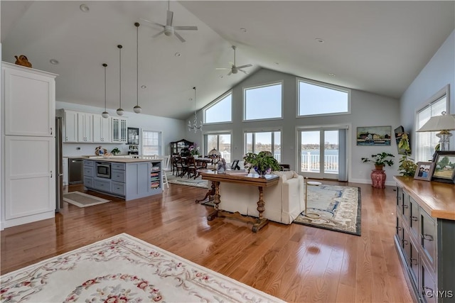 living area featuring a ceiling fan, high vaulted ceiling, a wealth of natural light, and light wood-type flooring
