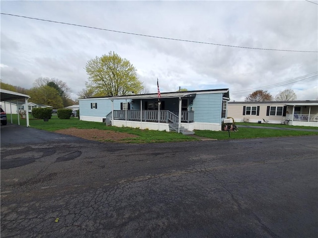 manufactured / mobile home featuring a porch, a front yard, a carport, and driveway