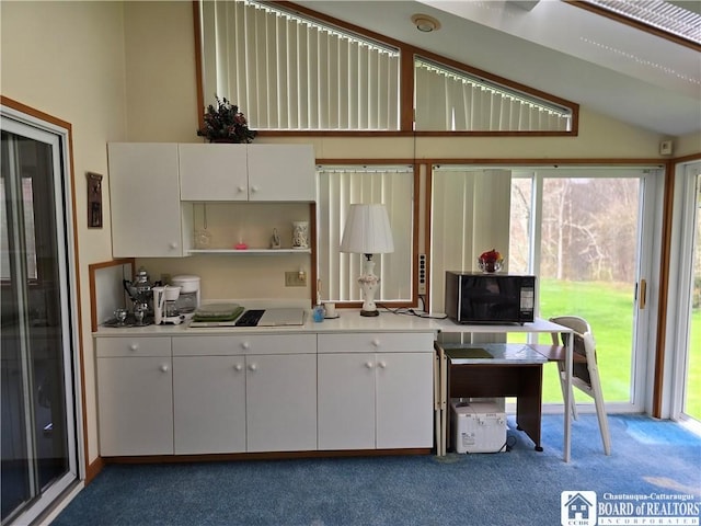kitchen featuring light countertops, black microwave, white cabinetry, vaulted ceiling, and carpet