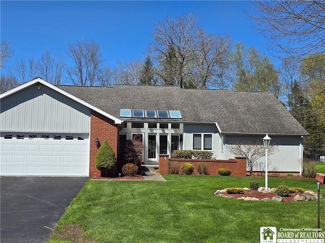 mid-century inspired home featuring a front lawn, a shingled roof, driveway, solar panels, and an attached garage