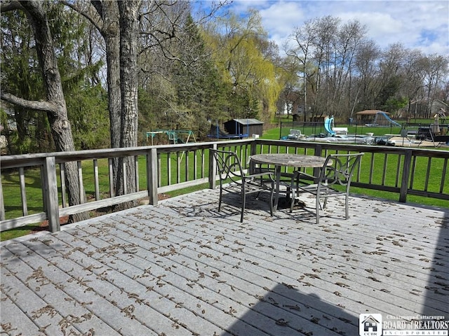 wooden terrace featuring an outdoor structure, a storage unit, outdoor dining space, and a playground