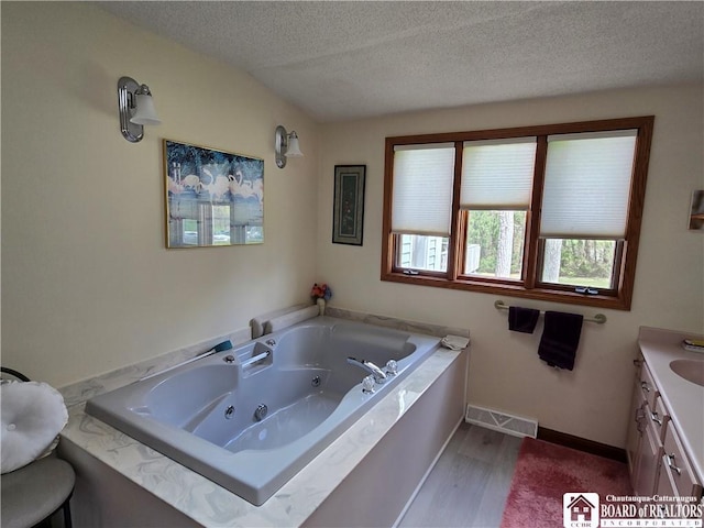 bathroom featuring a textured ceiling, visible vents, a jetted tub, wood finished floors, and vanity