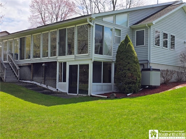 back of house with a sunroom, a lawn, and central AC