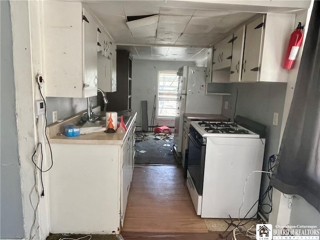 kitchen featuring white cabinets, wood finished floors, a sink, and white gas range