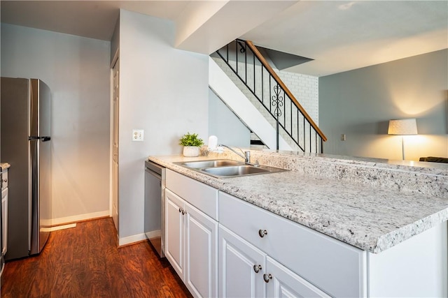 kitchen featuring white cabinets, a sink, appliances with stainless steel finishes, baseboards, and dark wood-type flooring