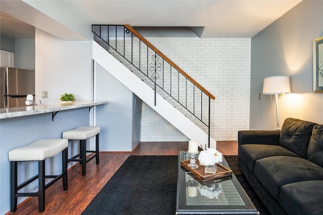 living room featuring dark wood-style floors, stairs, and brick wall
