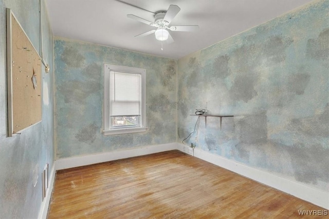 empty room with ceiling fan, wood finished floors, and baseboards