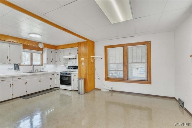 kitchen featuring white gas range oven, under cabinet range hood, light countertops, a sink, and baseboards