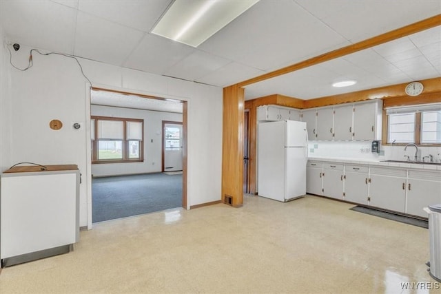 kitchen featuring light floors, freestanding refrigerator, a sink, baseboards, and visible vents