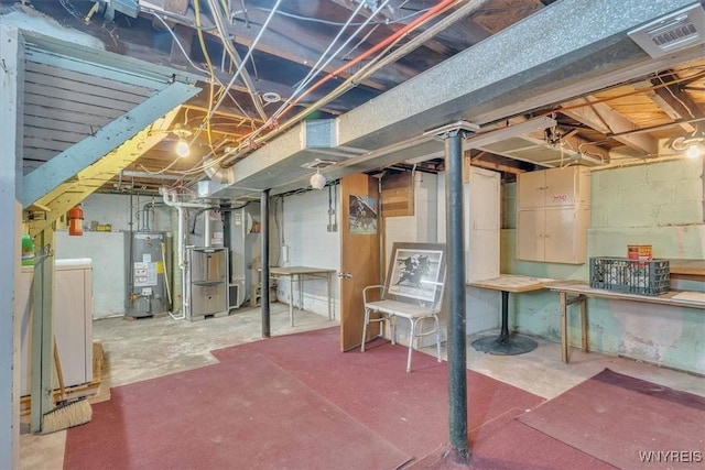unfinished basement with heating unit, visible vents, water heater, and washing machine and clothes dryer