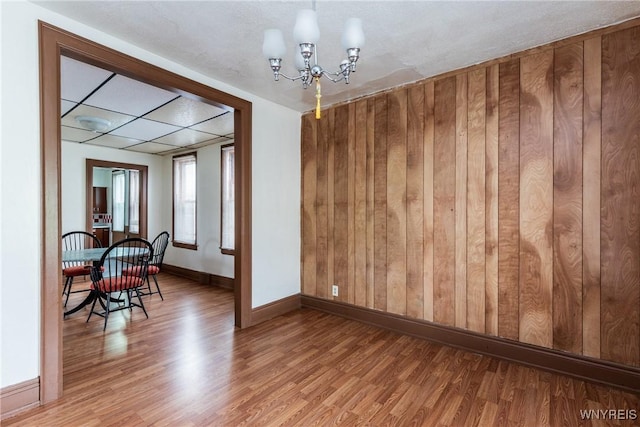 dining area featuring wooden walls, baseboards, wood finished floors, and a notable chandelier
