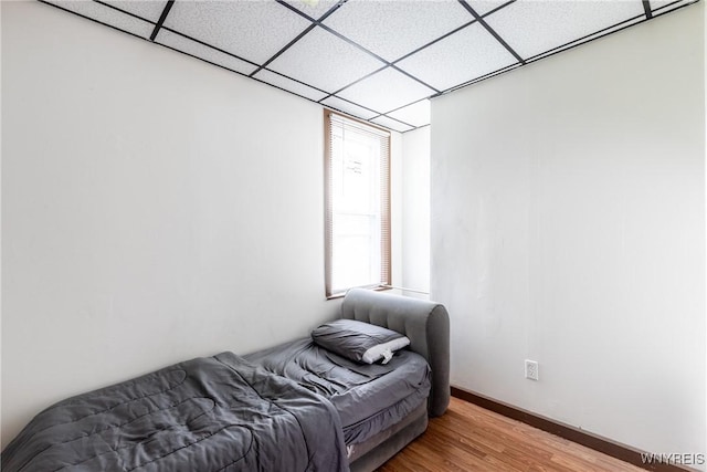 bedroom with baseboards, a drop ceiling, and light wood finished floors