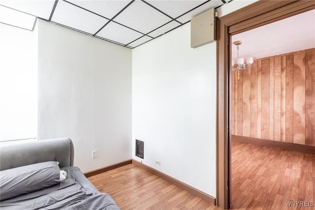 sitting room with wood walls, baseboards, a drop ceiling, a chandelier, and light wood finished floors