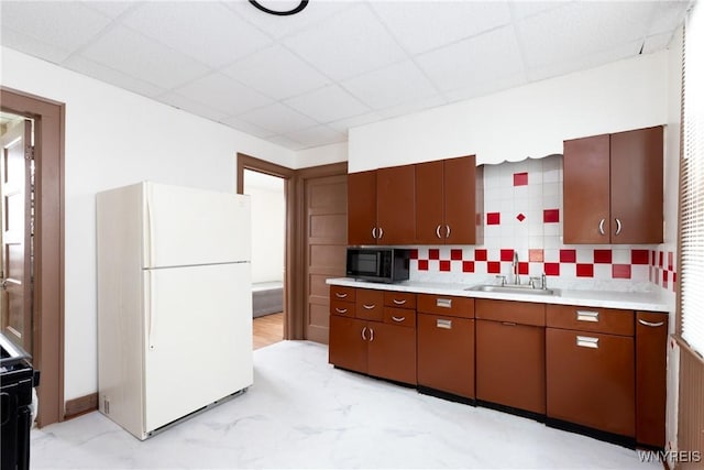 kitchen featuring a paneled ceiling, black microwave, light countertops, a sink, and freestanding refrigerator