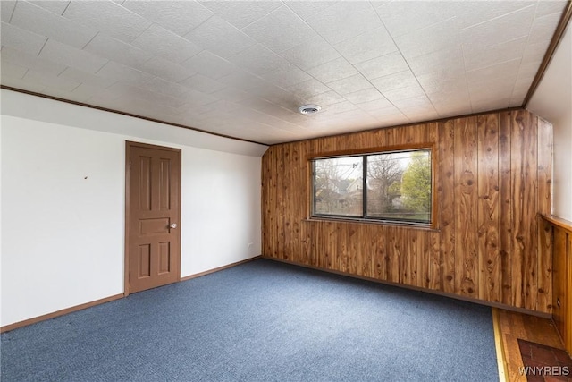 carpeted empty room with baseboards and wood walls