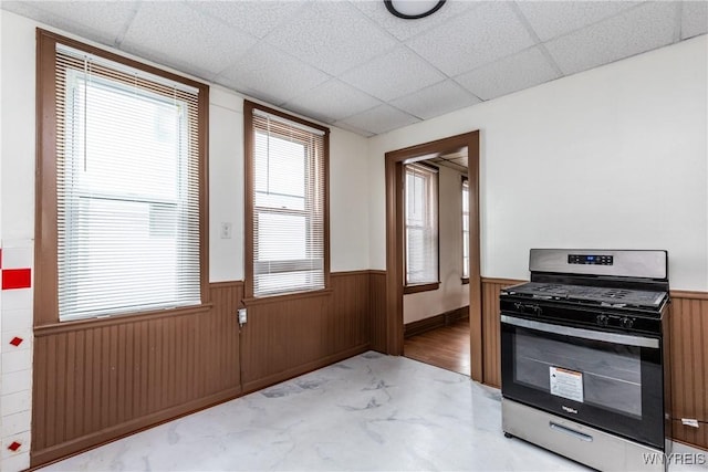 kitchen with wood walls, wainscoting, a drop ceiling, and stainless steel gas range