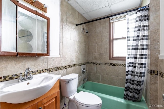 bathroom featuring vanity, shower / tub combo with curtain, toilet, tile walls, and a drop ceiling