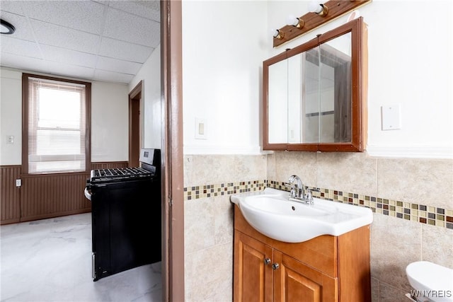bathroom featuring a wainscoted wall, vanity, toilet, and tile walls
