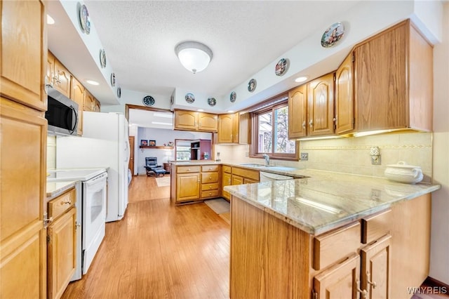 kitchen featuring stainless steel microwave, tasteful backsplash, light wood-type flooring, a peninsula, and white range with electric cooktop