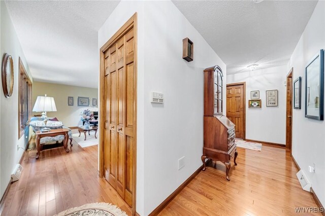 hallway featuring baseboards, visible vents, a textured ceiling, and light wood-style flooring