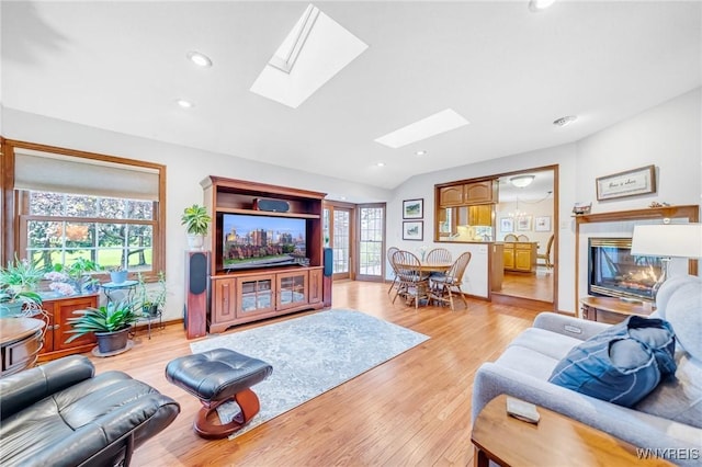 living room with a glass covered fireplace, vaulted ceiling with skylight, and light wood-type flooring