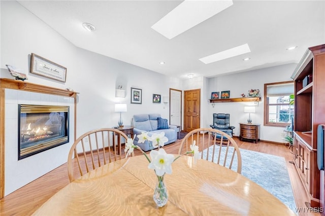 dining space with a tiled fireplace, recessed lighting, light wood-style flooring, and a skylight