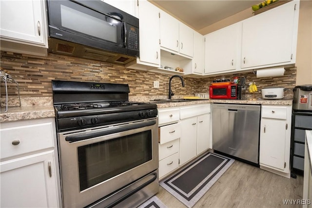 kitchen with light wood-style floors, appliances with stainless steel finishes, light countertops, white cabinets, and a sink