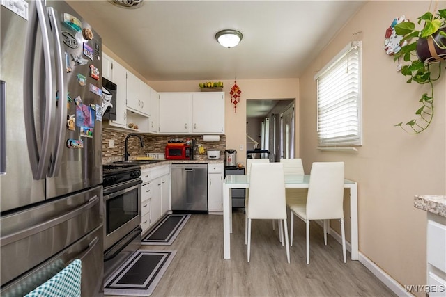 kitchen featuring decorative backsplash, appliances with stainless steel finishes, light wood finished floors, a sink, and white cabinetry