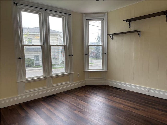 empty room featuring visible vents, baseboards, and dark wood-type flooring