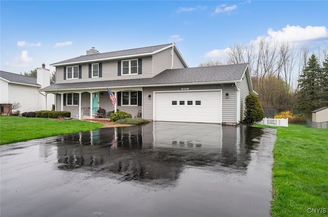 traditional-style home featuring a front yard, an attached garage, covered porch, and aphalt driveway