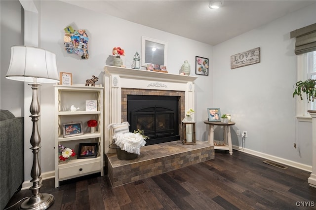 living room with baseboards, visible vents, wood finished floors, and a brick fireplace