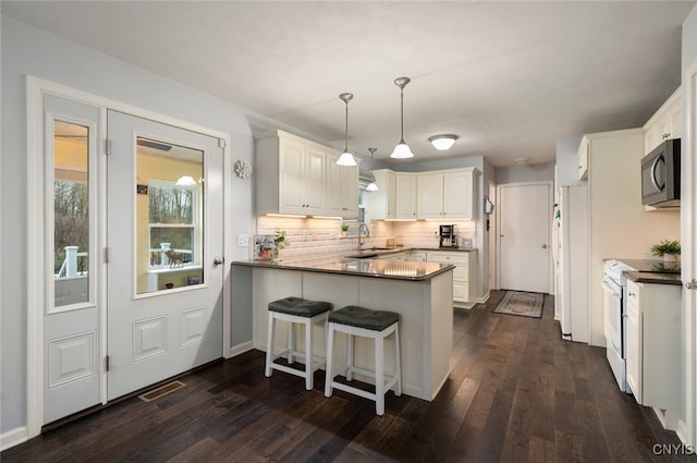 kitchen featuring dark wood-style floors, a sink, a peninsula, and white appliances