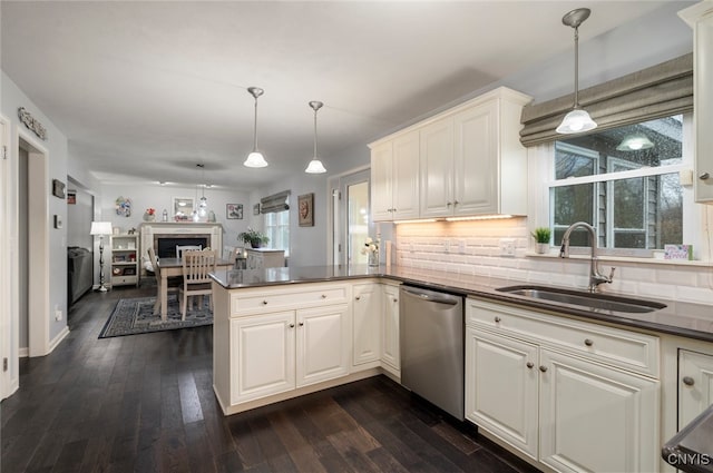 kitchen with dark wood-style floors, a sink, a peninsula, stainless steel dishwasher, and dark countertops