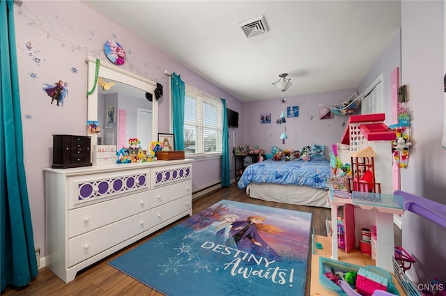 bedroom with baseboard heating, visible vents, and wood finished floors